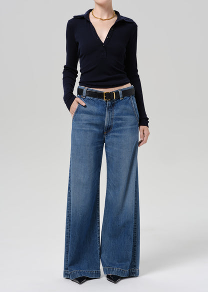 Person wearing blue polo sweater and blue pants on a grey background