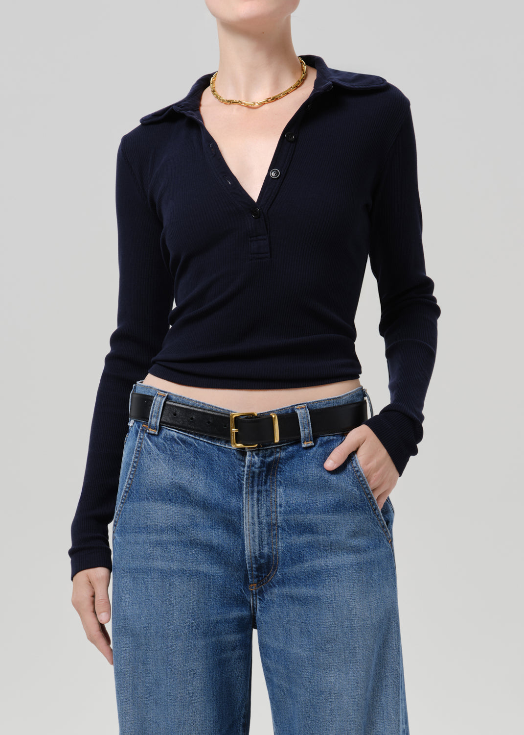 Person wearing blue polo sweater and blue pants on a grey background