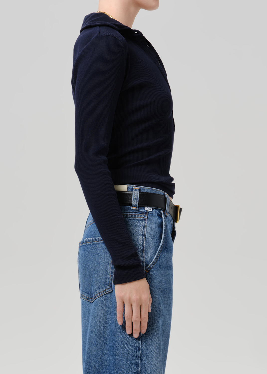 Person wearing blue polo sweater and blue pants on a grey background