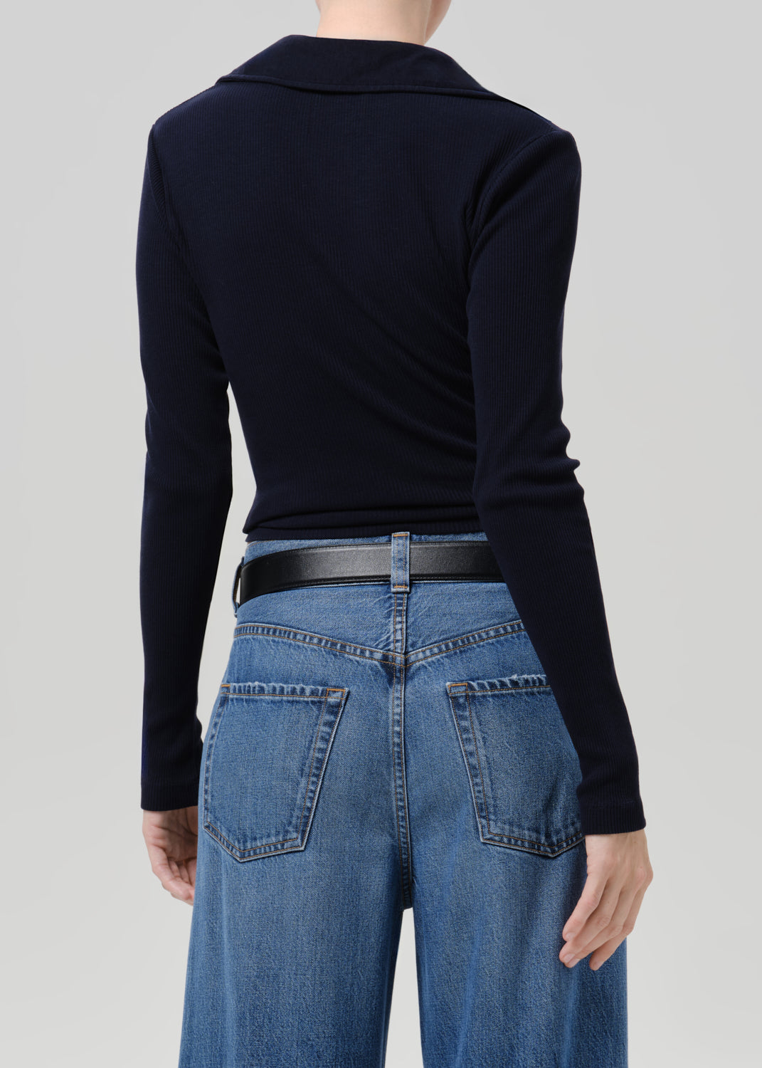 Person wearing blue polo sweater and blue pants on a grey background
