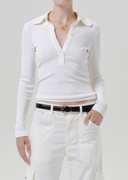 Person wearing white polo top with white pants on a grey background