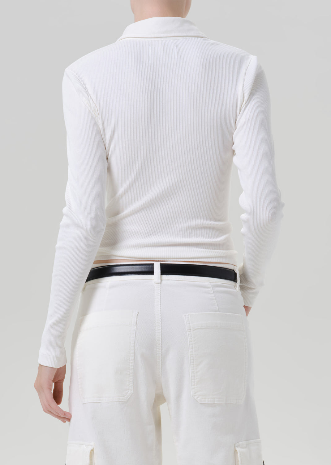 Person wearing white polo top with white pants on a grey background