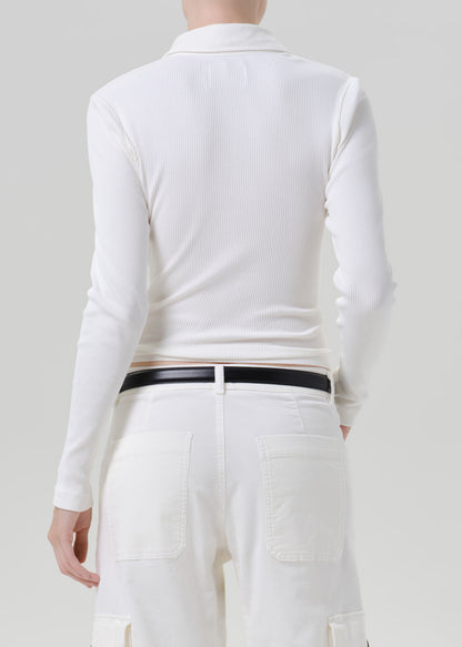 Person wearing white polo top with white pants on a grey background