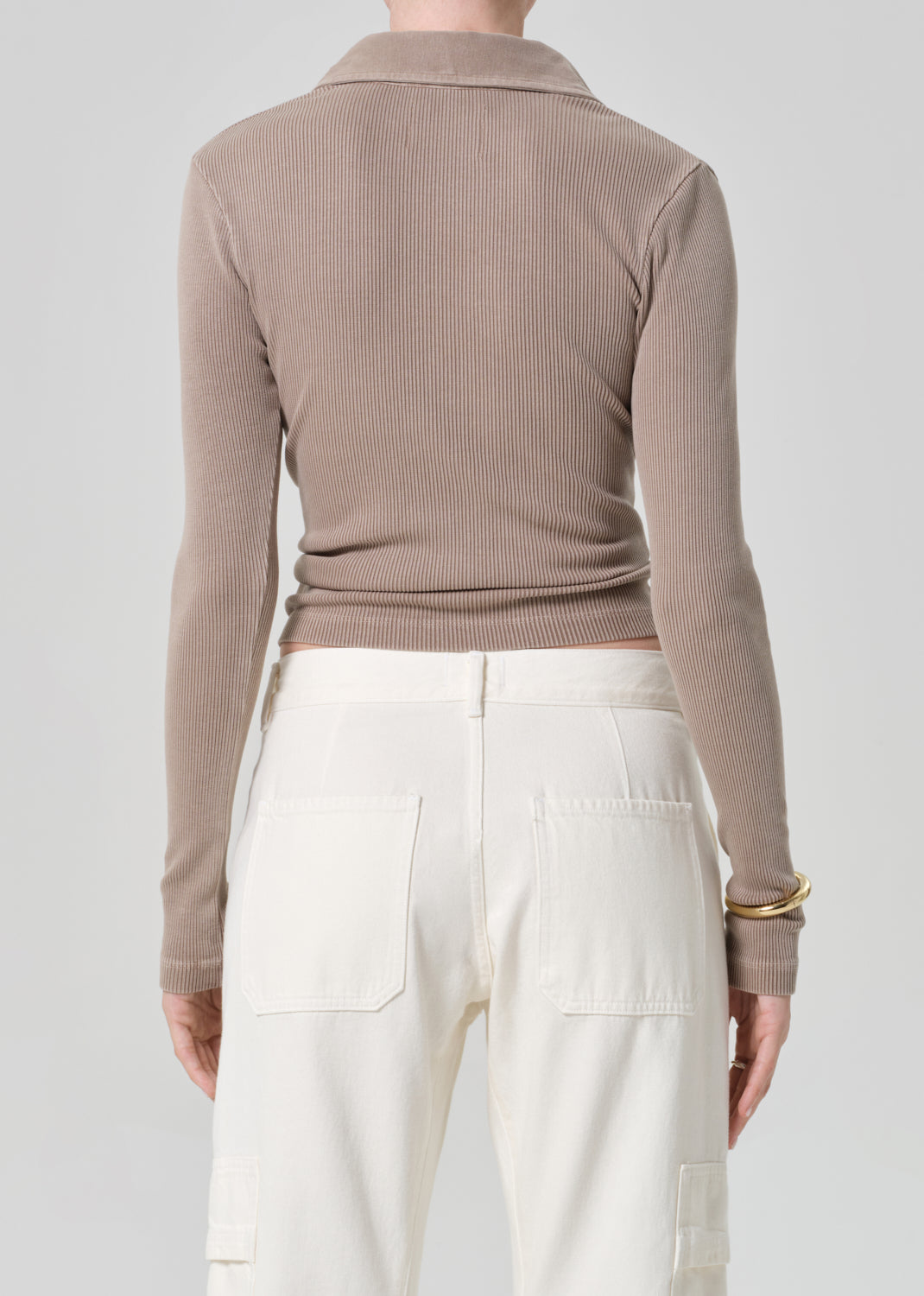 Person wearing a brown ribbed long-sleeve polo and white pants on a light gray background