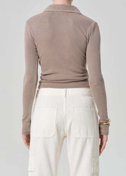 Person wearing a brown ribbed long-sleeve polo and white pants on a light gray background