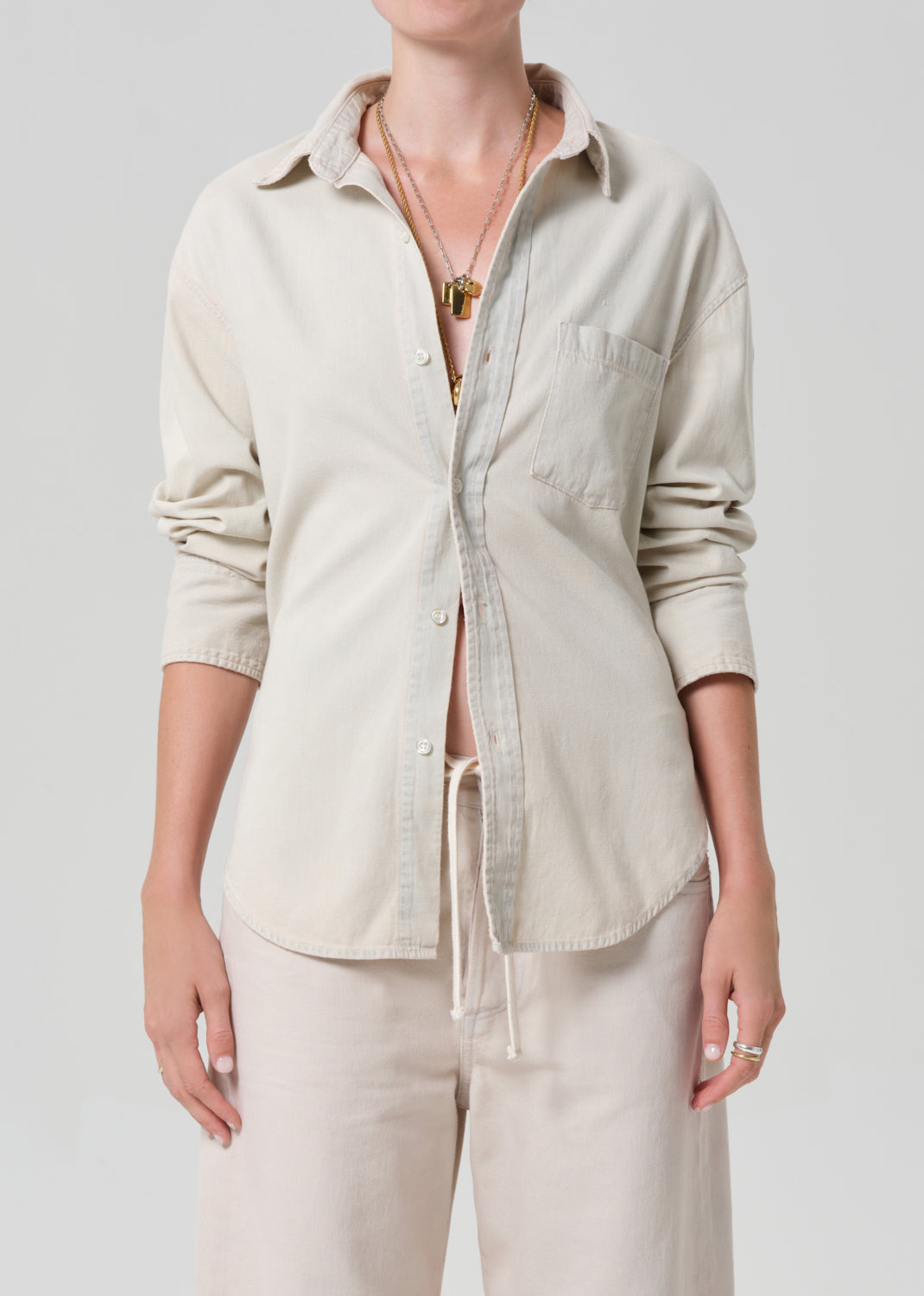 Person wearing a beige button-up shirt and pants on a plain background