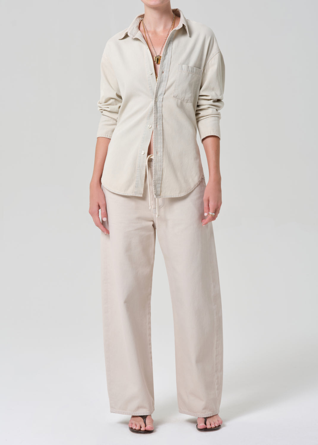 Person wearing a beige shirt and pants on a grey background