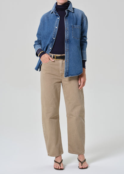 Person wearing a denim shirt, black turtleneck, beige pants, and sandals on a white background