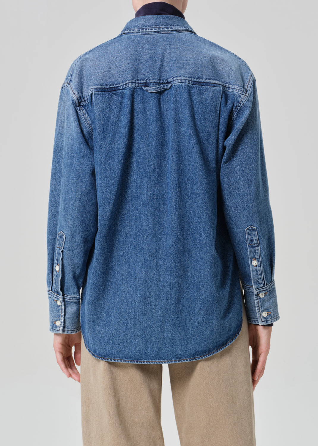 Blue denim shirt worn by a person on a plain background