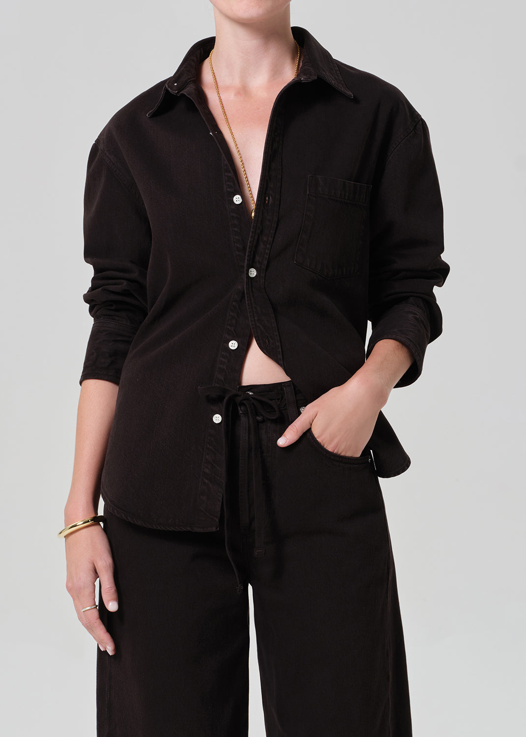 Person wearing a brown  button-up shirt and brown pants on a plain background