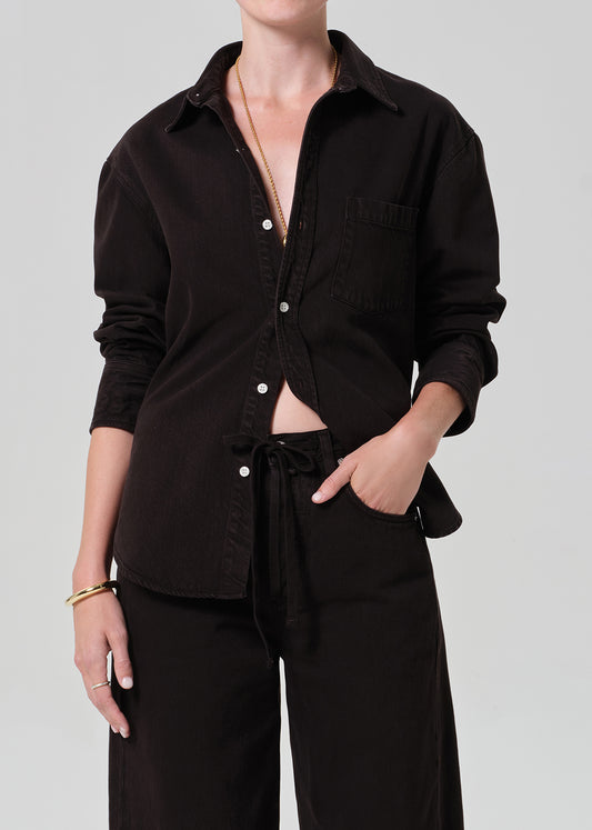 Person wearing a brown  button-up shirt and brown pants on a plain background