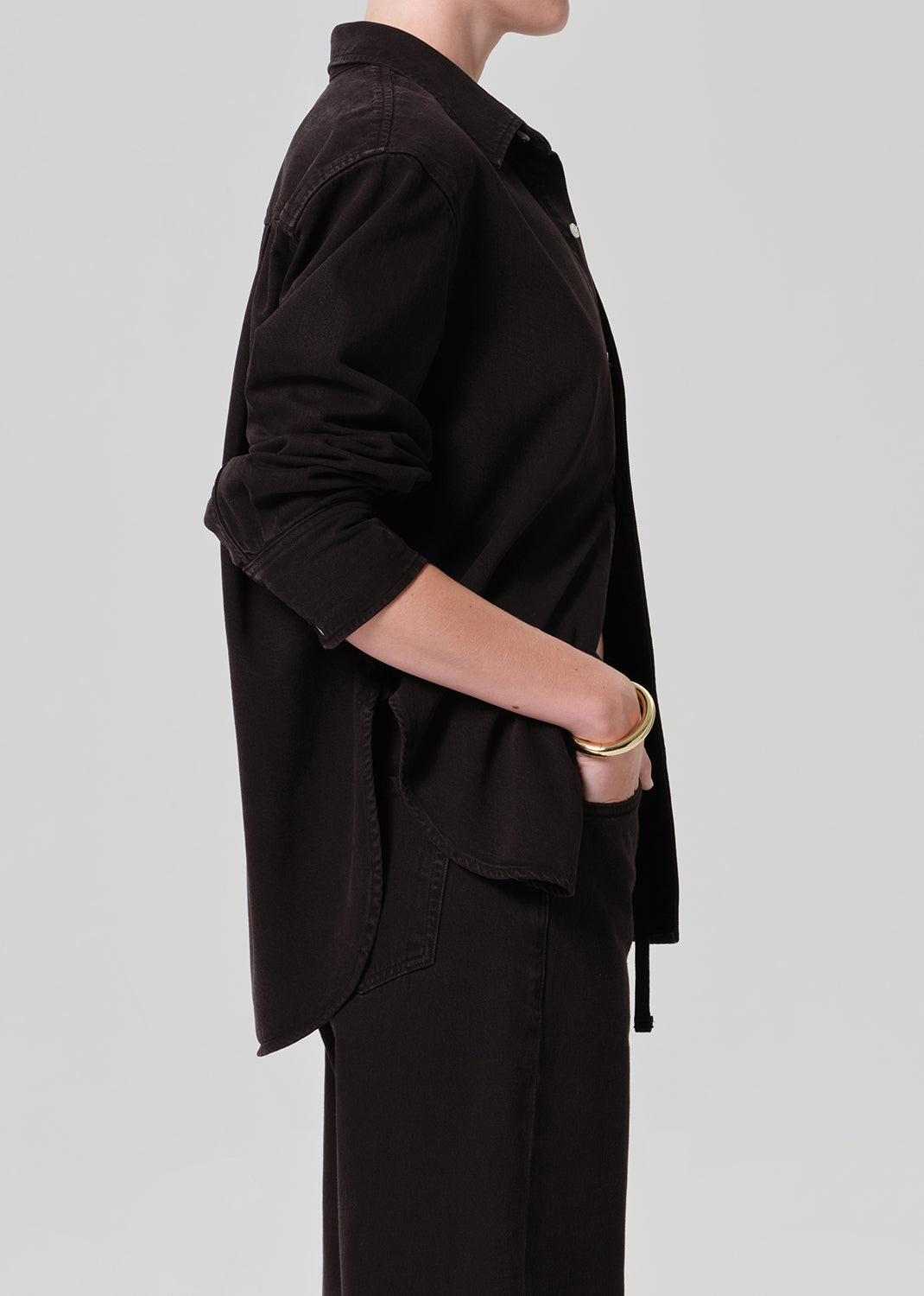 Person wearing a brown  button-up shirt and brown pants on a plain background