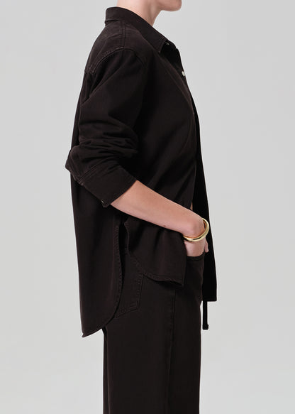 Person wearing a brown  button-up shirt and brown pants on a plain background