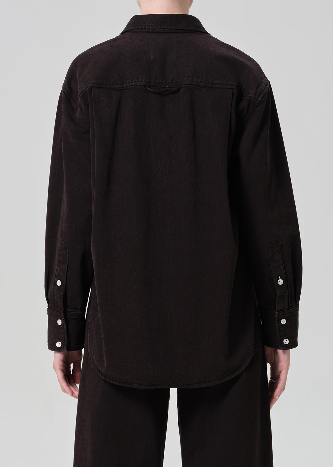 Person wearing a brown  button-up shirt and brown pants on a plain background