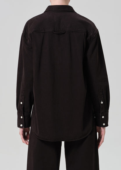 Person wearing a brown  button-up shirt and brown pants on a plain background