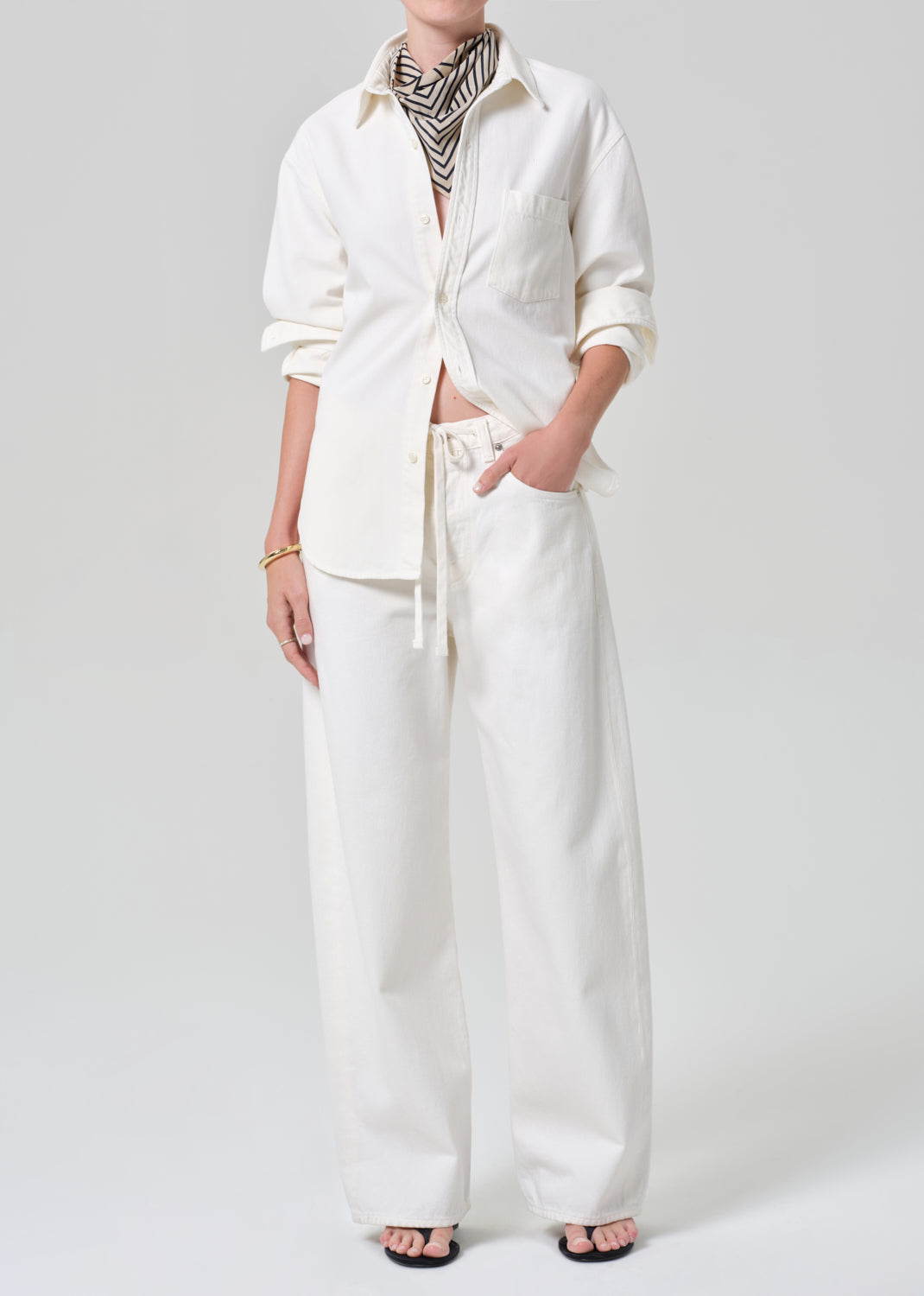 Person wearing a white shirt and matching wide leg pants with a striped scarf on a plain background