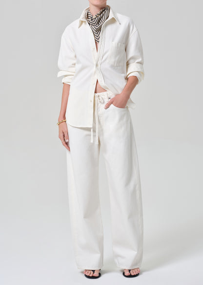 Person wearing a white shirt and matching wide leg pants with a striped scarf on a plain background