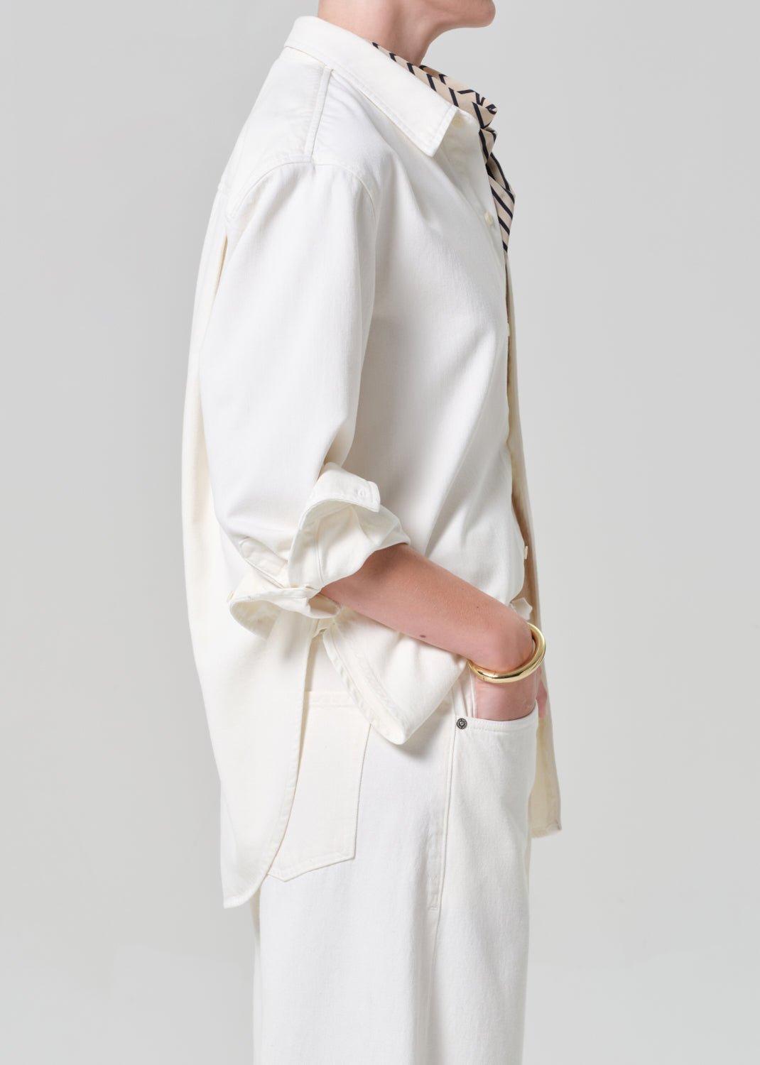 Person wearing a white shirt and matching wide leg pants with a striped scarf on a plain background