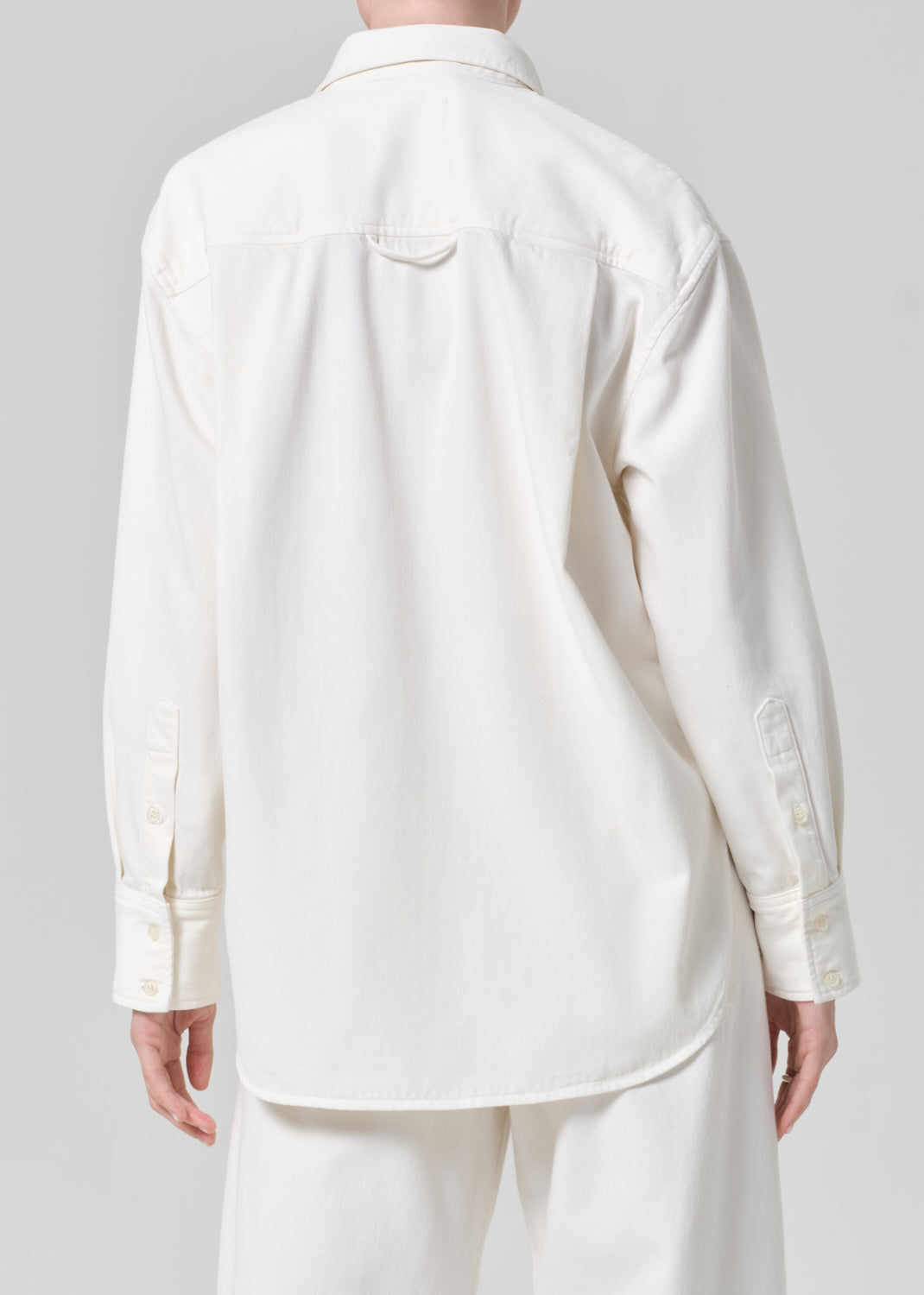 Person wearing a white shirt and matching wide leg pants with a striped scarf on a plain background