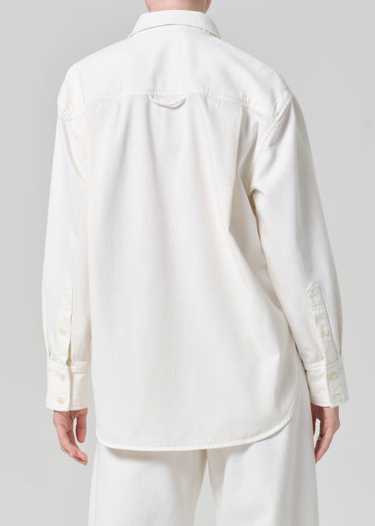 Person wearing a white shirt and matching wide leg pants with a striped scarf on a plain background