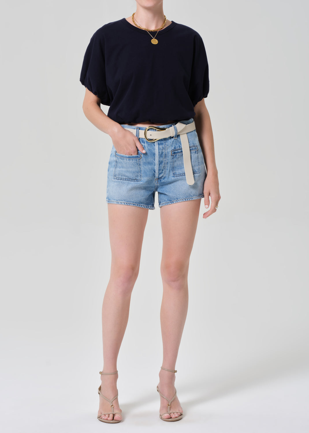 Person wearing a navy t-shirt and denim shorts on a plain background