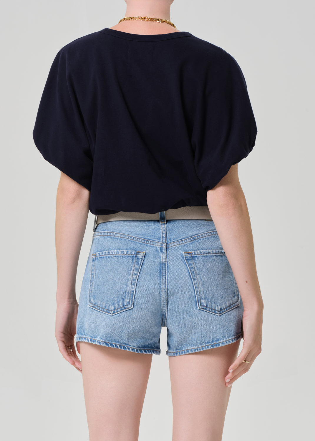 Person wearing a navy top and light blue denim shorts on a plain background