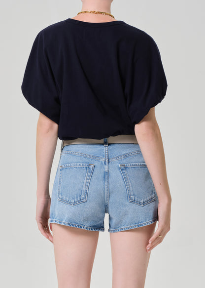 Person wearing a navy top and light blue denim shorts on a plain background