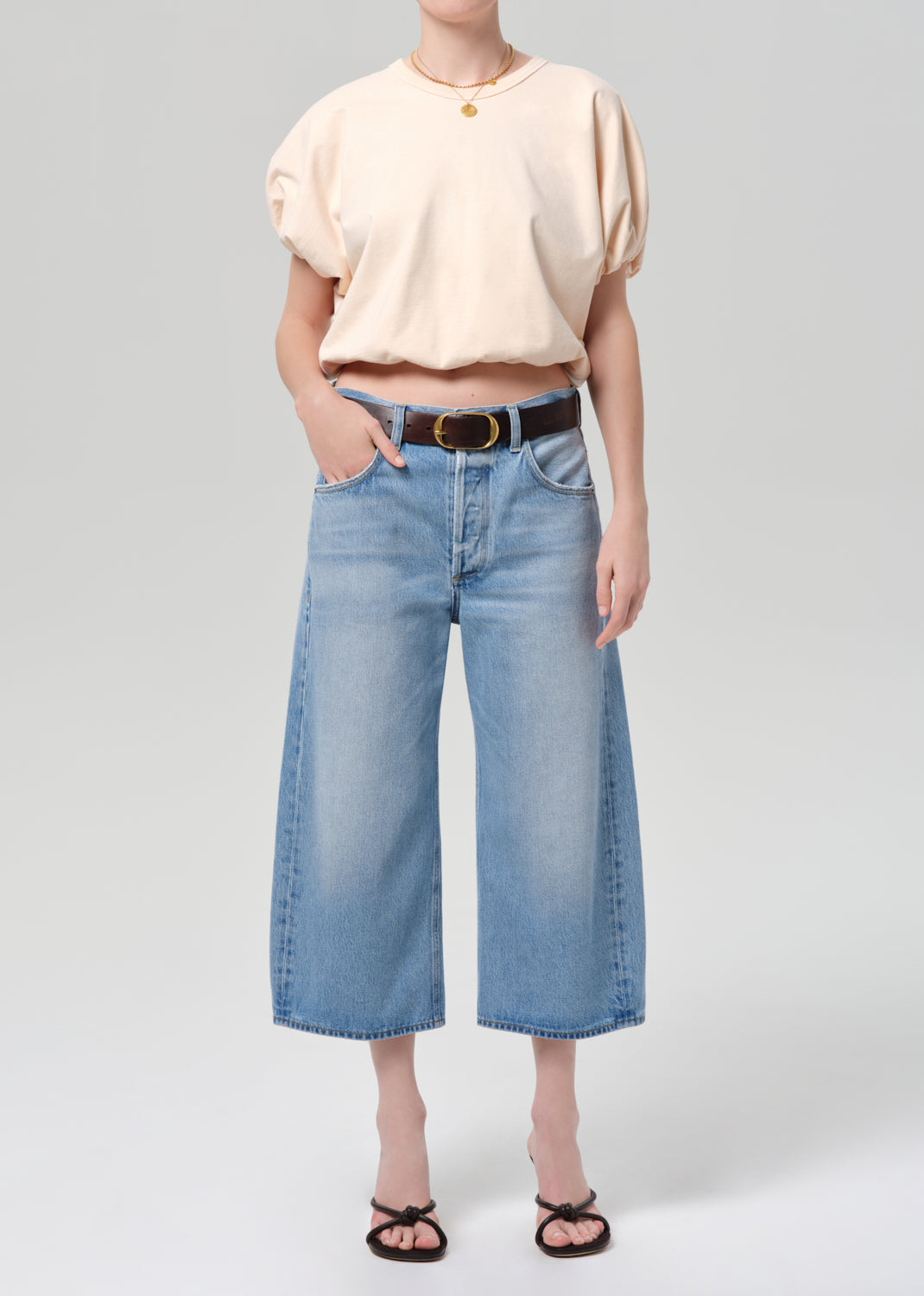 Person wearing a light coral top and blue jeans with a belt on a gray background