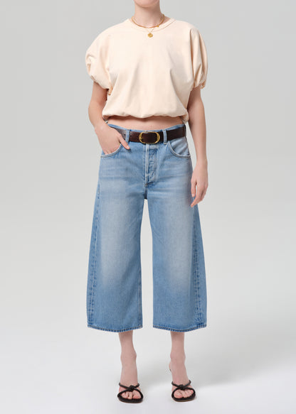 Person wearing a light coral top and blue jeans with a belt on a gray background