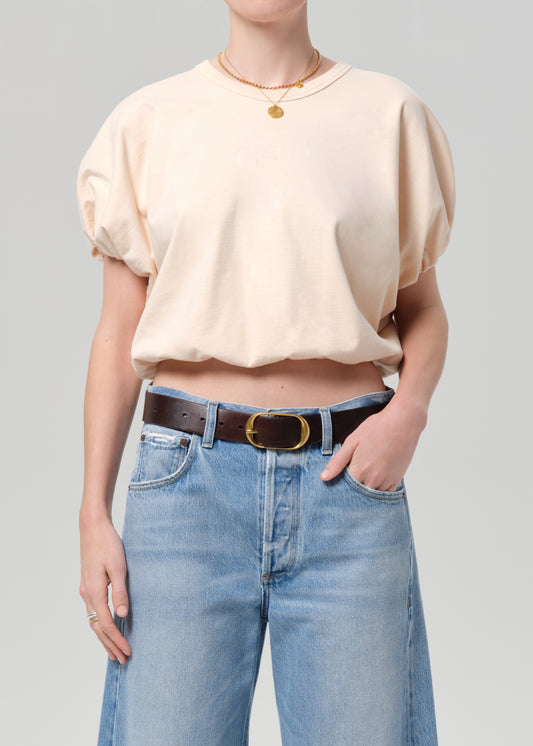 Person wearing a light coral top and blue jeans with a belt on a gray background