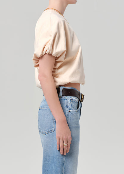 Person wearing a light coral top and blue jeans with a belt on a gray background