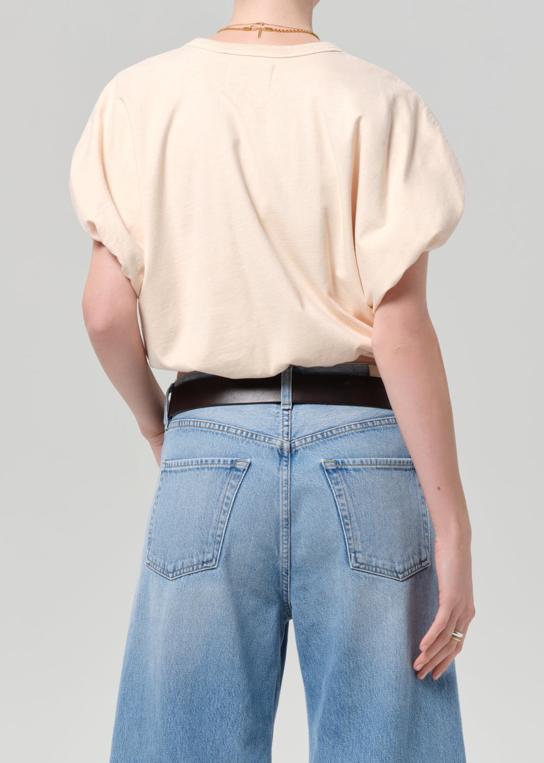 Person wearing a light coral top and blue jeans with a belt on a gray background