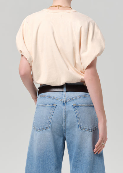 Person wearing a light coral top and blue jeans with a belt on a gray background