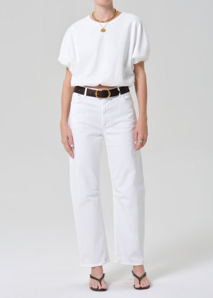 Person wearing a white top and white pants with a belt on a plain background