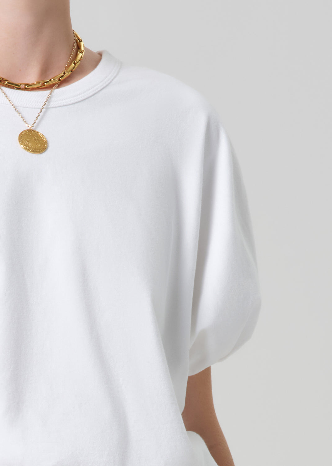 White t-shirt worn by a person with gold necklaces on a plain background