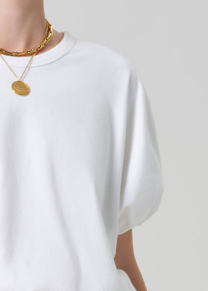 White t-shirt worn by a person with gold necklaces on a plain background
