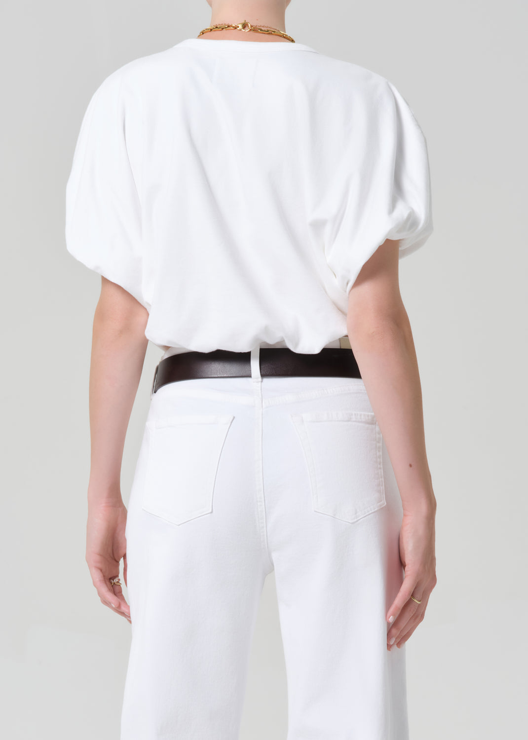 Person wearing a white blouse and white pants with a black belt on a plain background