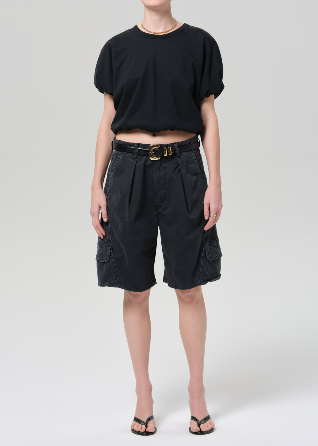 Person wearing a black top and dark cargo shorts on a plain background