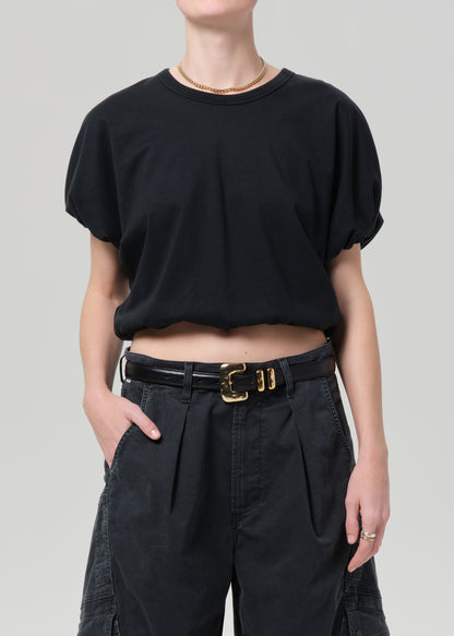 Person wearing a black crop top and black pants with a belt on a gray background