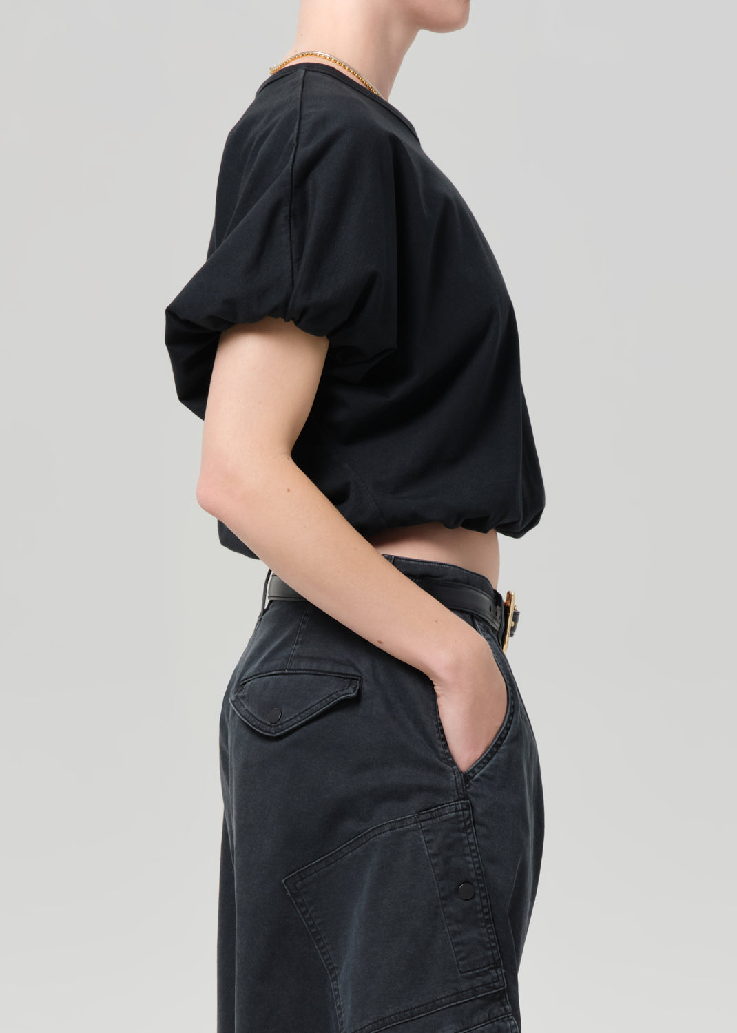 Person wearing a black top and dark pants on a light gray background