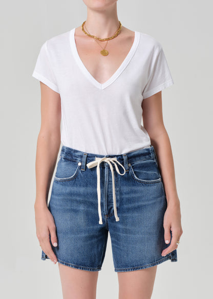 Person wearing a white t-shirt and blue denim shorts on a plain background