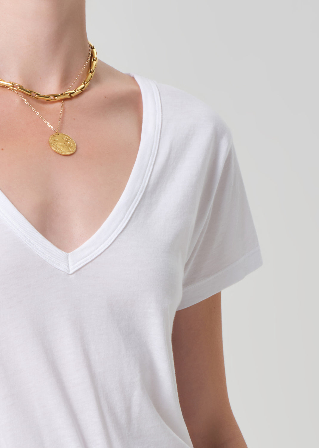 White t-shirt worn by a person with a gold necklace on a plain background