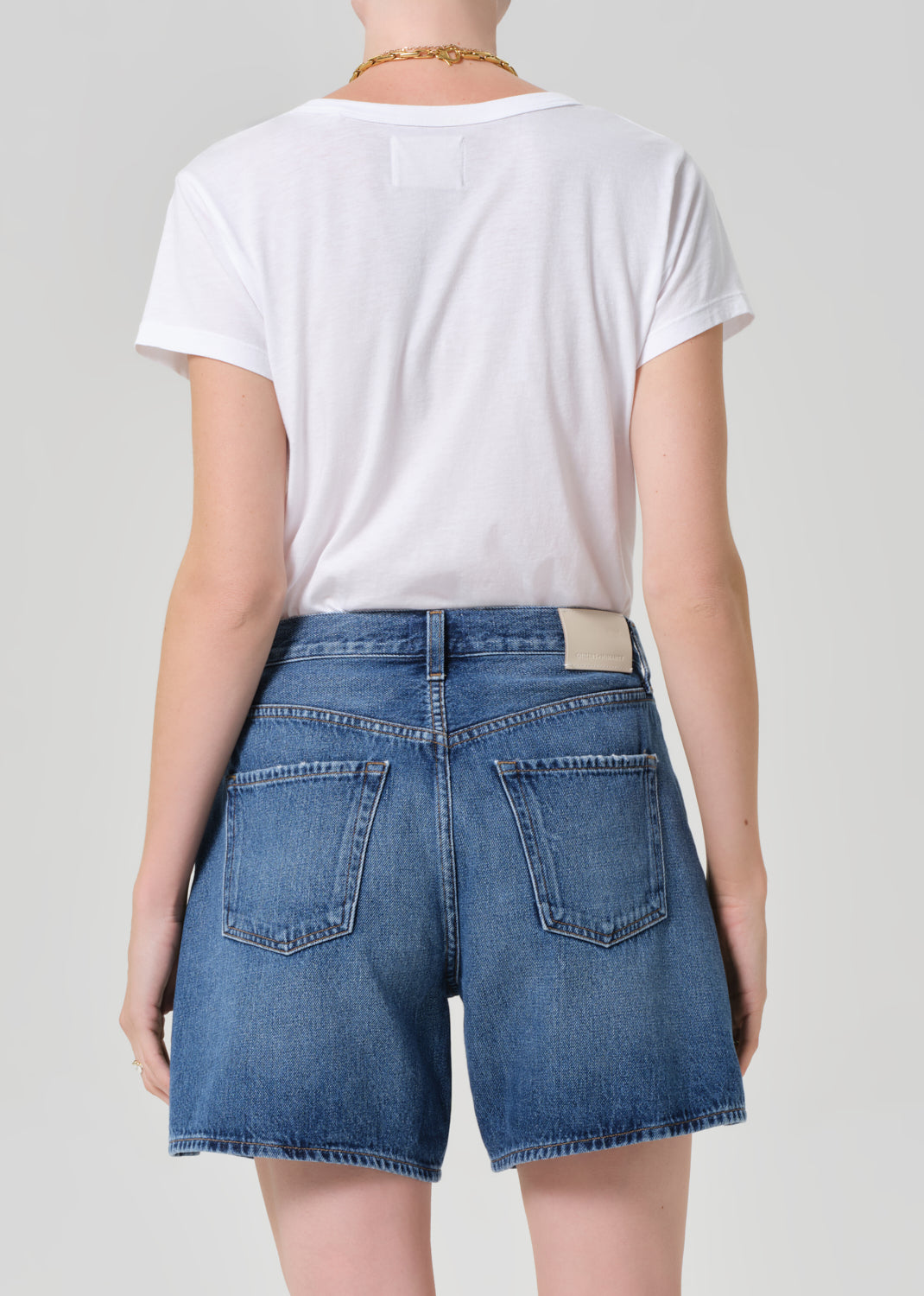 Person wearing a white t-shirt and blue denim shorts on a plain background