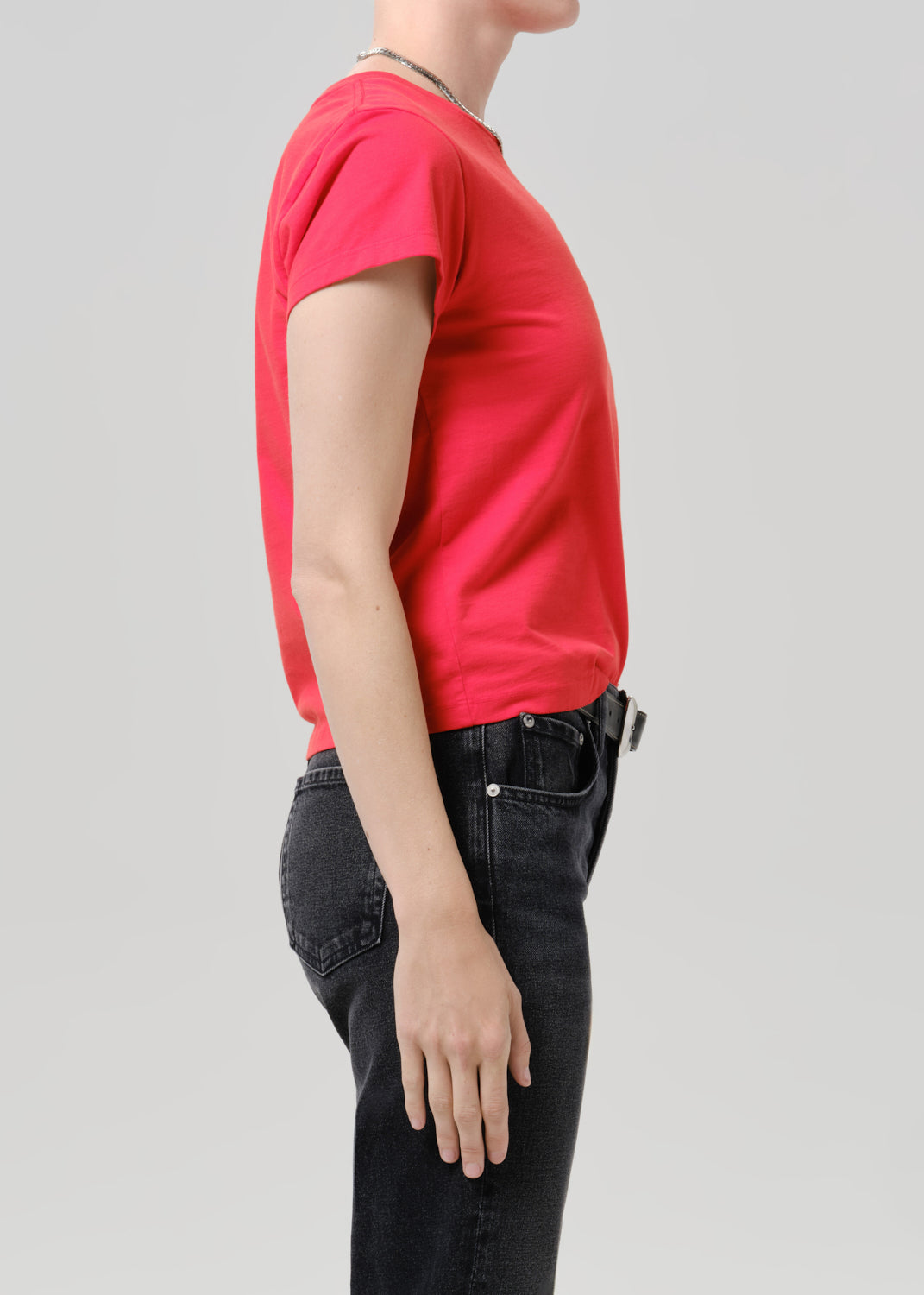 Person wearing red t-shirt with dark pants on a grey background