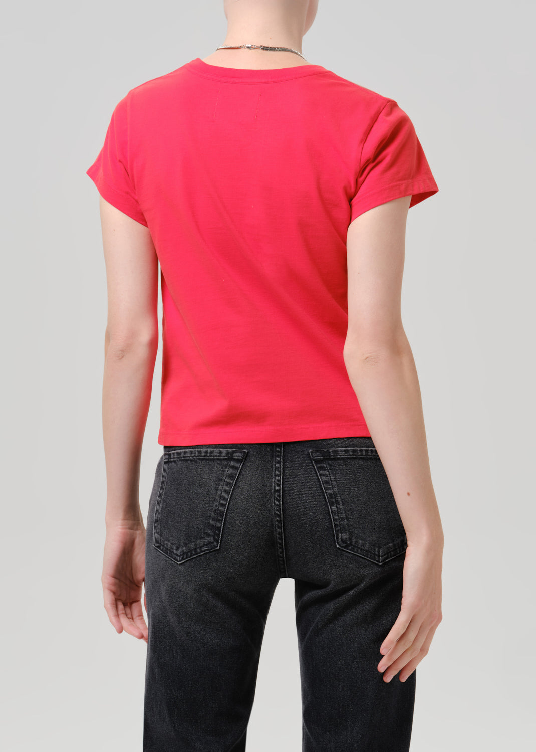 Person wearing red t-shirt with dark pants on a grey background