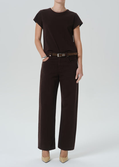 A model wearing a dark brown short-sleeve top and matching dark brown wide-leg trousers with a brown belt, paired with beige pointed-toe heels, against a grey background.
