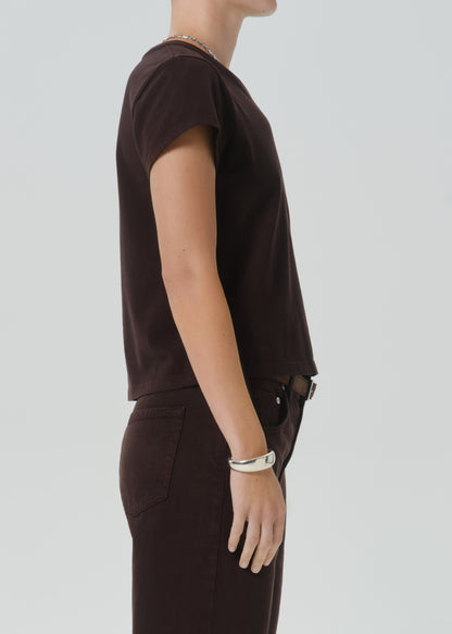 A side-profile view of a person wearing a dark brown short-sleeve crewneck t-shirt and matching dark brown pants against a grey background.