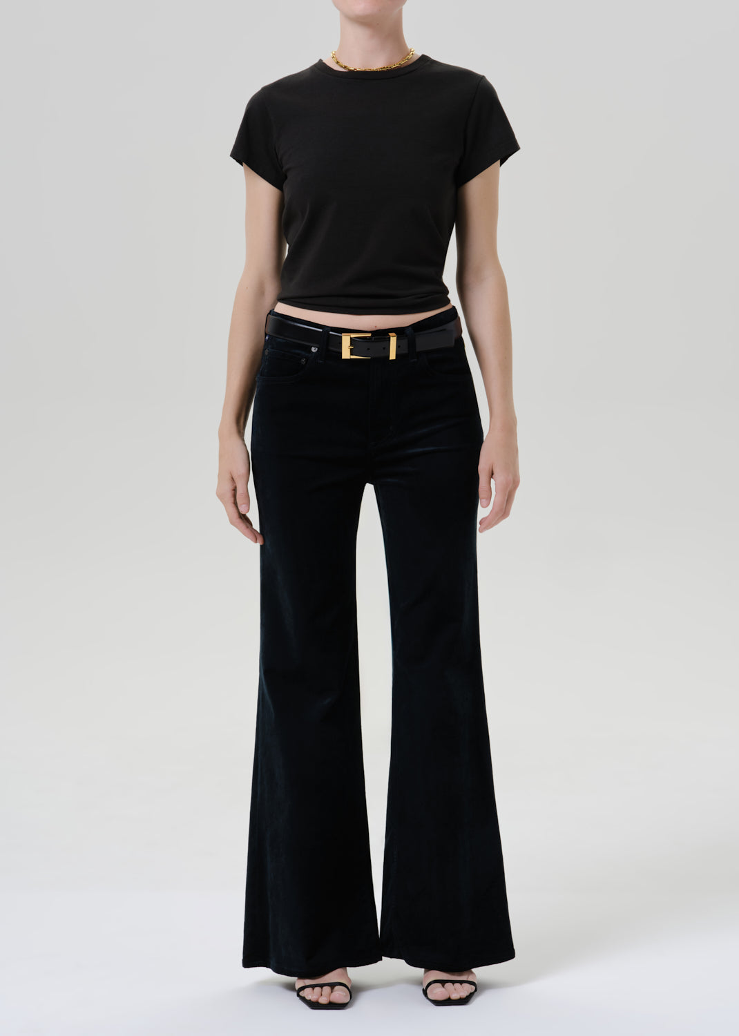 Person wearing a black short sleeve crewneck tee with black wide leg jeans and black sandals on a grey background
