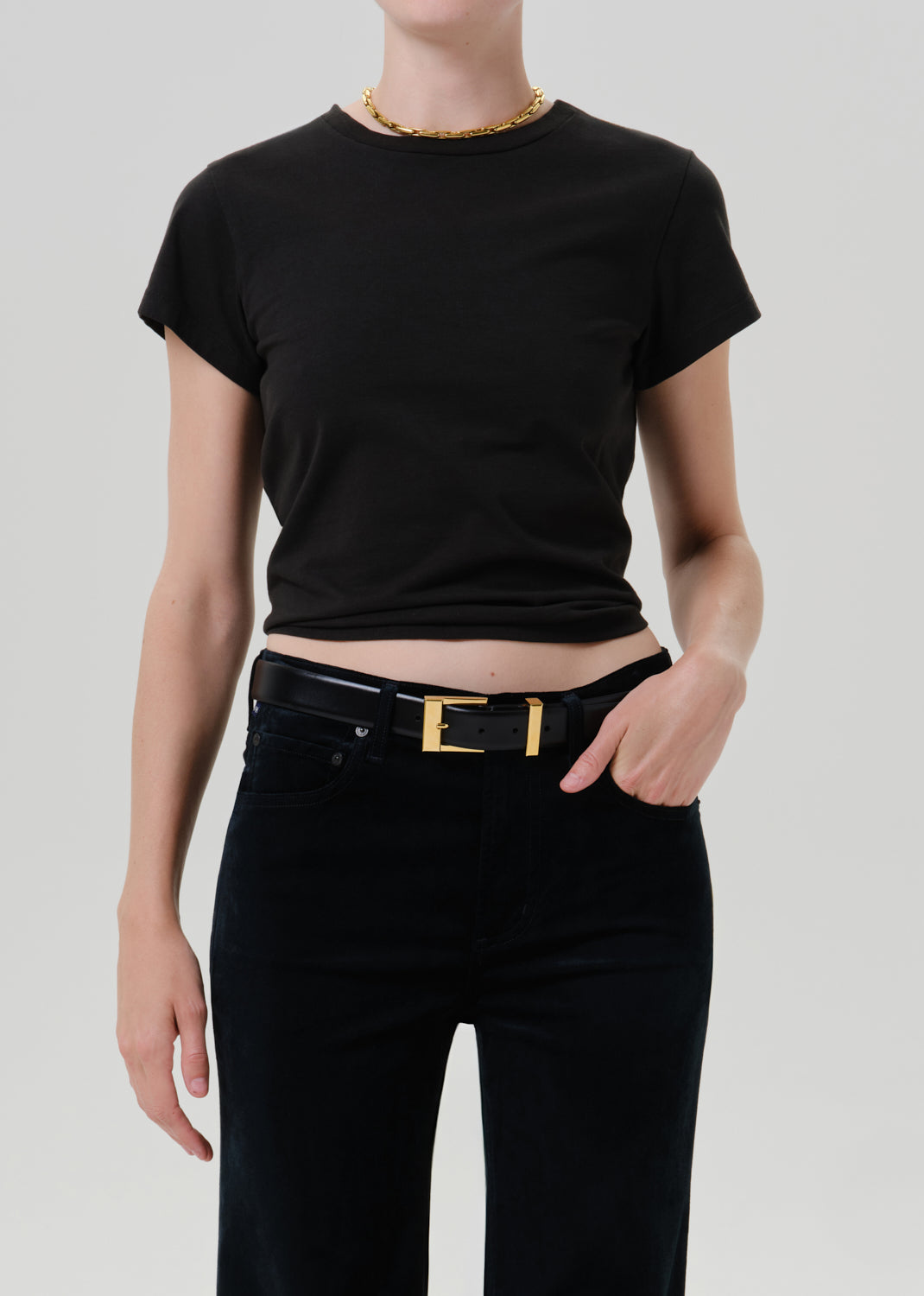 Person wearing a black short sleeve crewneck tee with black wide leg jeans on a grey background