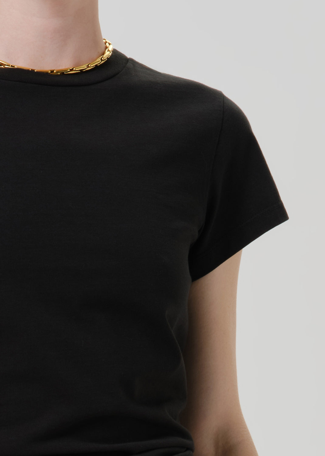 Person wearing a black short sleeve crewneck tee on a grey background